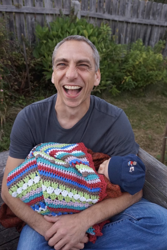andererseits-Unterstützer Björn sitzt in einem Garten. Er lacht und hält ein Baby auf dem Arm.